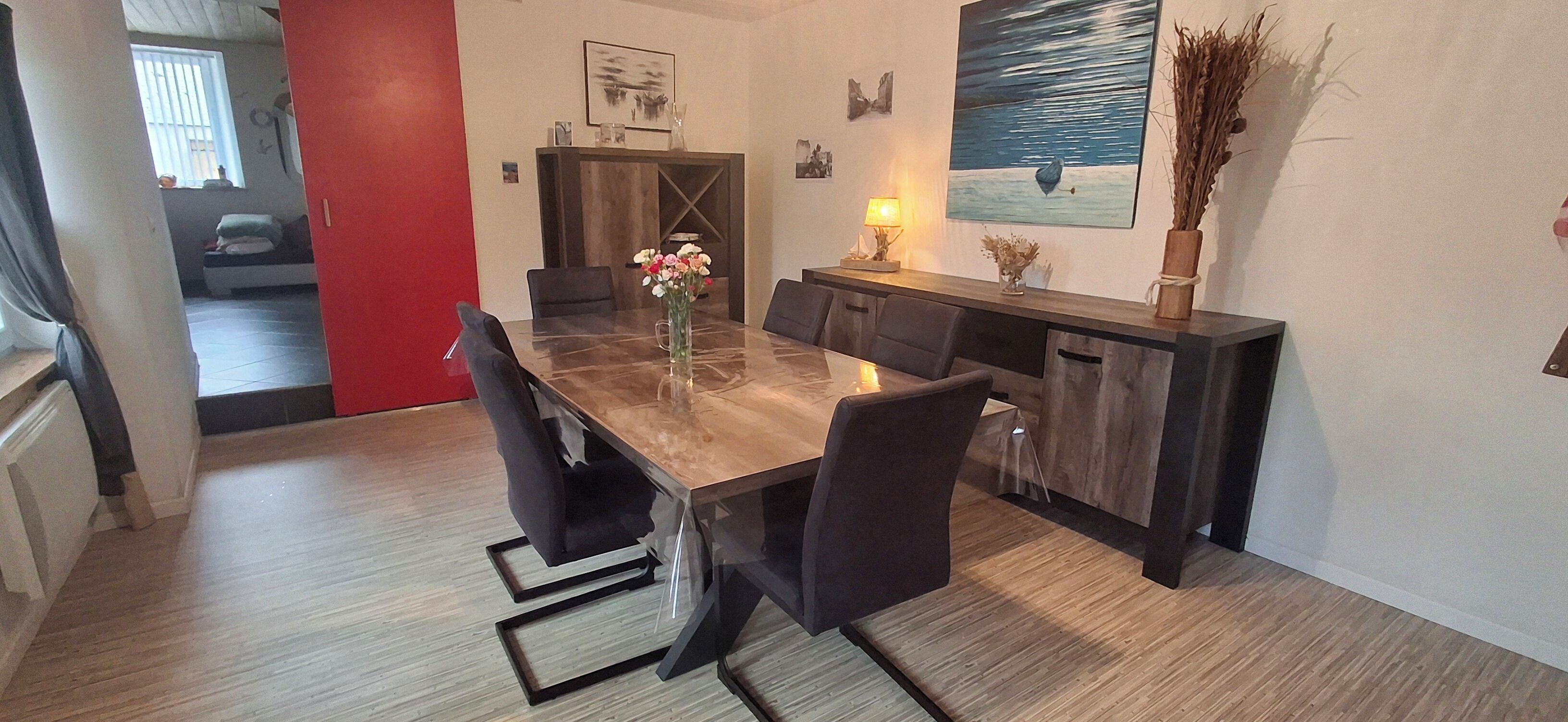 A dining area with a marble table, black chairs, and a vase of flowers. There is a wooden sideboard with a lamp and a painting on the wall.