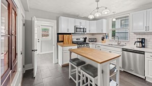 A modern kitchen with white cabinets, stainless steel appliances, and a wooden island with bar stools. - Spacious Downtown Retreat w/ Private Yard & Mountain Views (Colorado Springs)