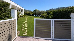 Una casa moderna con fachada blanca, un sendero pavimentado que conduce a una zona verde y vistas del paisaje circundante.