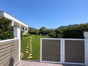 Ein modernes Haus mit weißer Fassade, einem gepflasterten Weg, der zu einer Rasenfläche führt, und Blick auf die umliegende Landschaft.