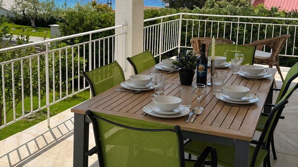 Mesa de madera dispuesta para comer, con sillas, vista al mar y una barandilla blanca.