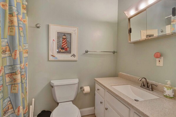 Un baño con inodoro, lavamanos, toallero y un cuadro con una imagen de un faro.