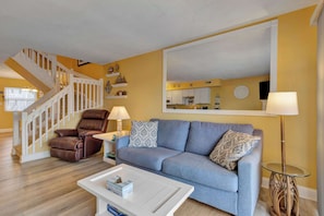 Ein Wohnzimmer mit Sofa, Couchtisch, Relaxsessel, Lampe und einer Treppe.