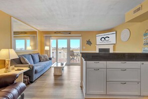 Una sala moderna con sofá, mesa de centro y comedor. Hay una cocina con armarios blancos y un cartel de Ocean City Vacation Homes.