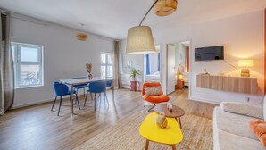 Ein modernes Wohnzimmer mit Essbereich, einer Couch, einem an der Wand befestigten Fernseher und einem großen Fenster.