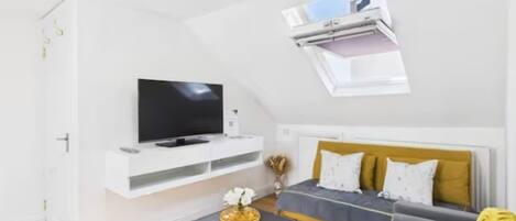 A modern living room with a flat-screen TV on a white console, a sofa with yellow cushions, and a small table with a decorative item.