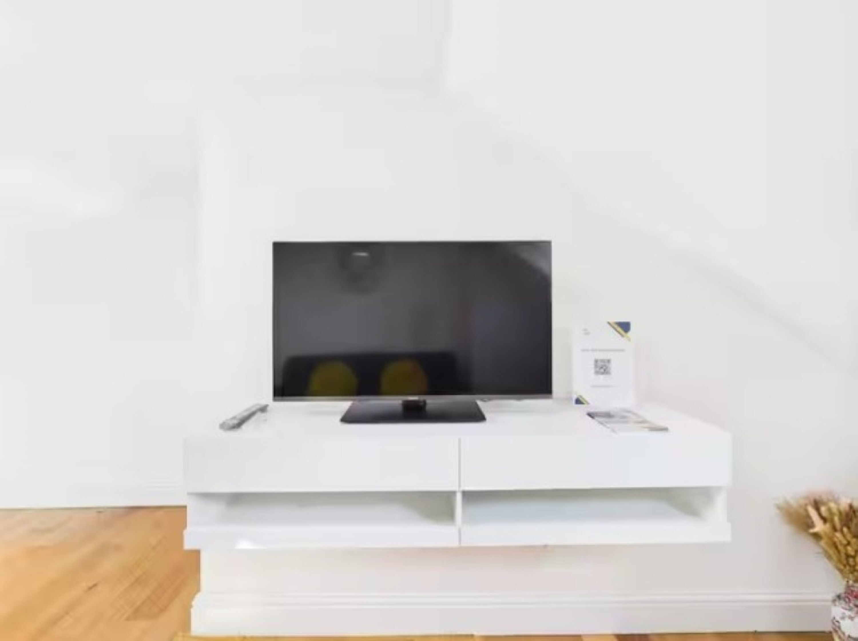 A white entertainment unit with a flat-screen TV, remote controls, and a QR code.