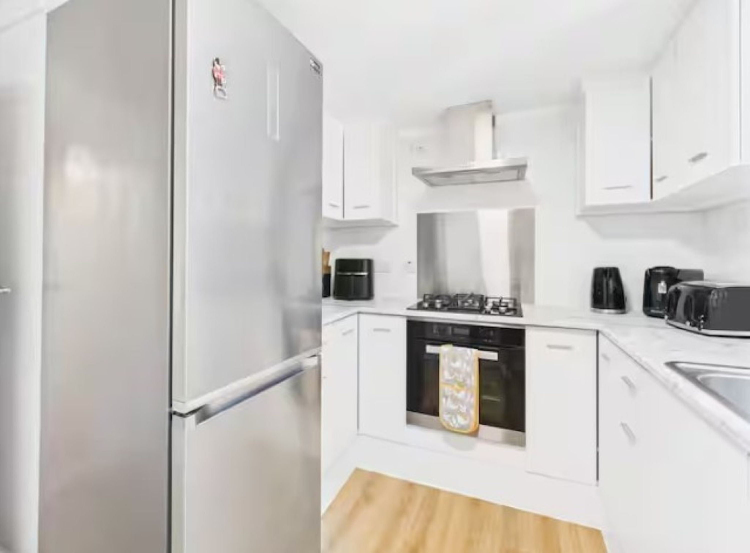 A modern kitchen with white cabinets, a stainless steel refrigerator, a stove, and a coffee maker.
