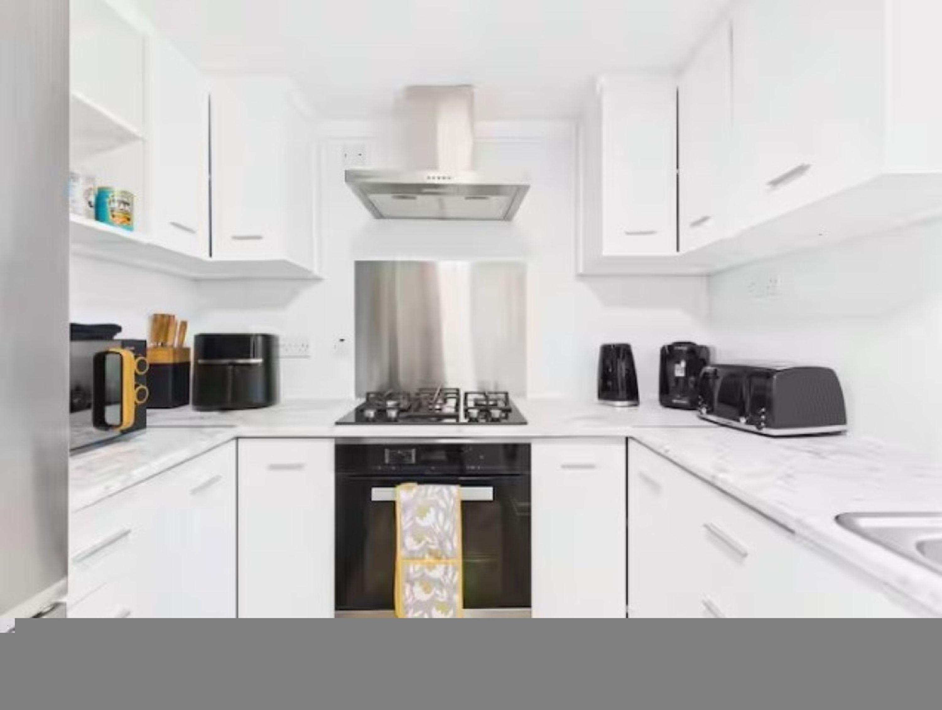 A modern kitchen with white cabinets, a gas stove, a range hood, a coffee maker, and a toaster.
