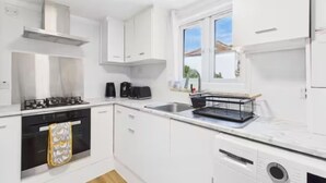 A modern kitchen with white cabinets, a gas stove, a coffee maker, and a window with a view. - 4BR London Home Piccadilly Line Sleeps 9 (London)