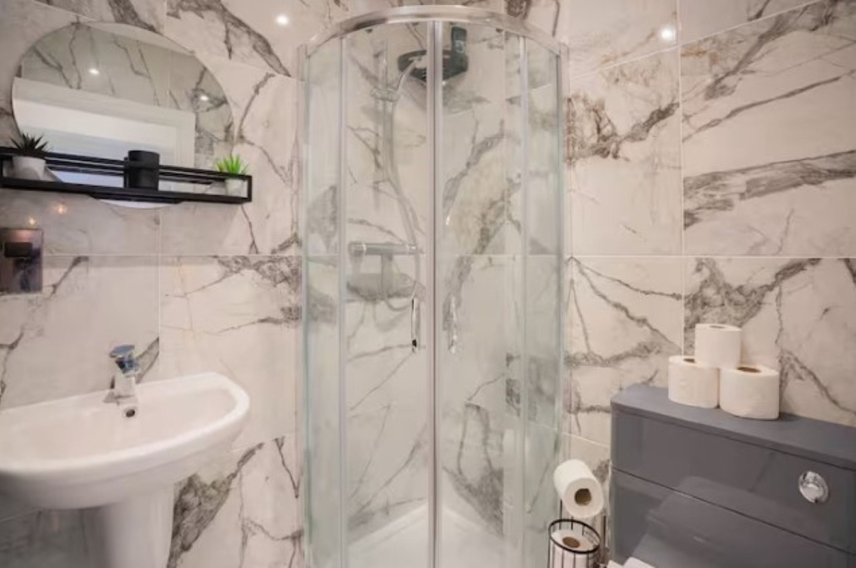 Ein Badezimmer mit Duschkabine aus Glas, einem Waschbecken und Marmorwänden.