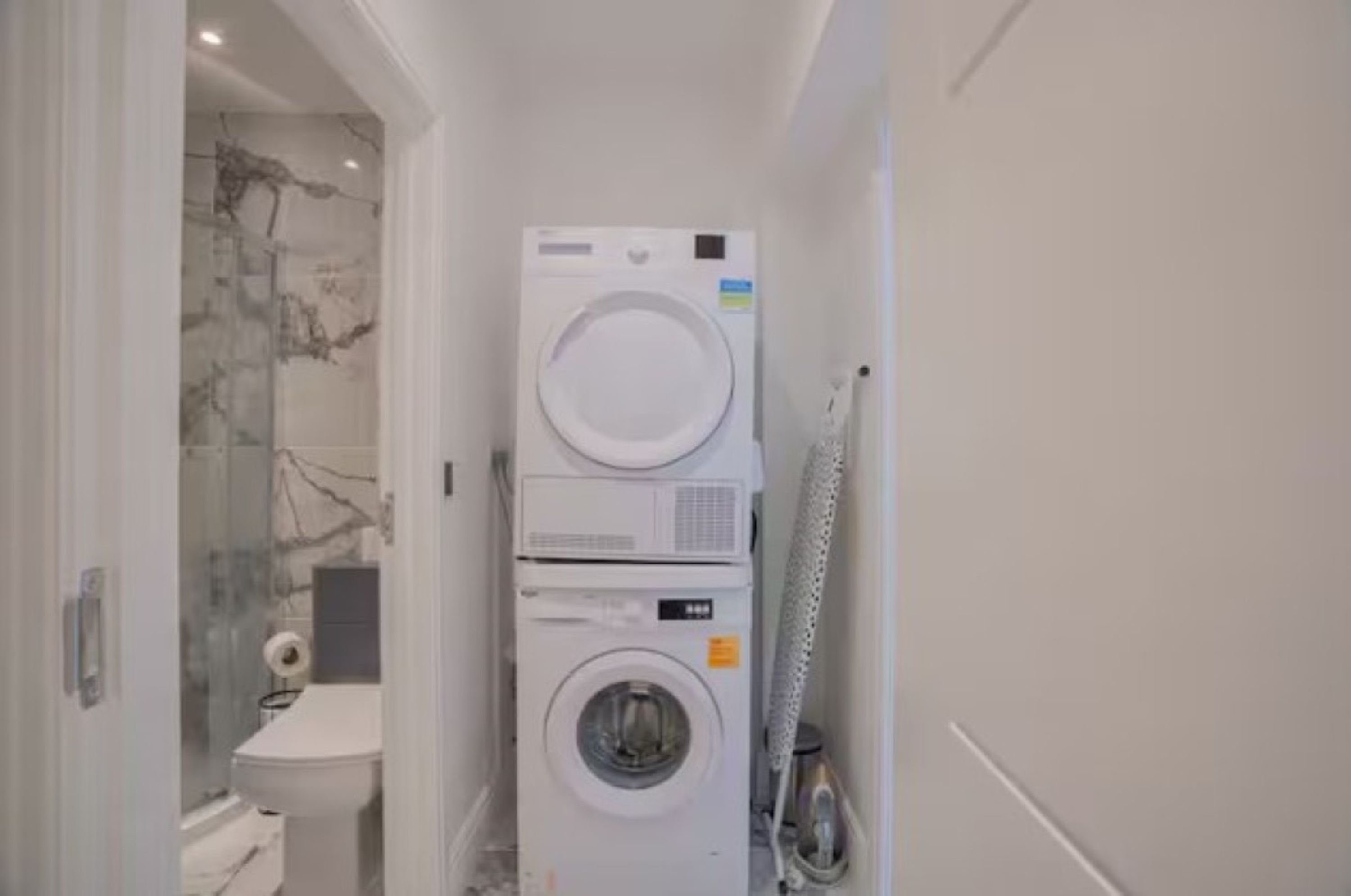 A compact laundry area with a stacked washer and dryer, a glass shower enclosure, and a toilet.