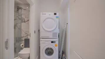 A compact laundry area with a stacked washer and dryer, a glass shower enclosure, and a toilet.