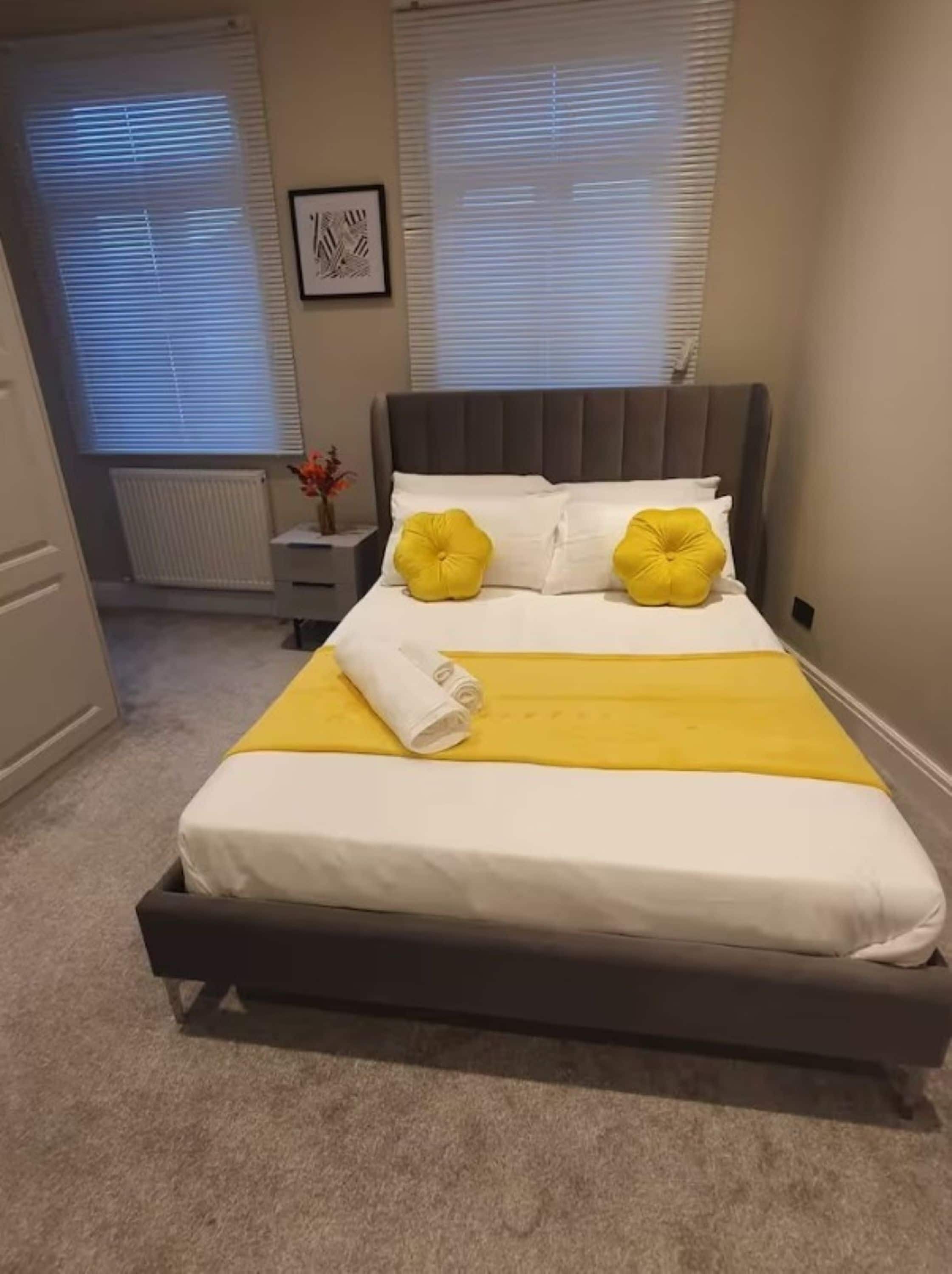 Ein ordentlich gemachtes Bett mit grauem Kopfteil, weißer Bettwäsche und zwei gelben Kissen.