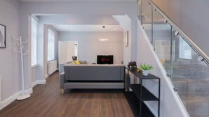 Una sala de estar moderna con un sofá gris, una mesita con adornos y una escalera con barandillas de cristal.
