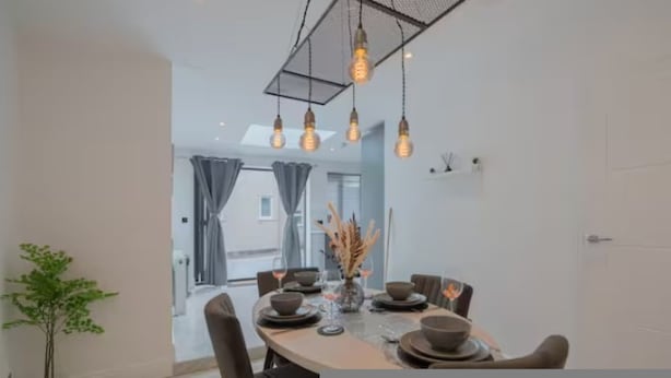 Un comedor moderno con una mesa redonda dispuesta para cuatro personas, iluminación colgante y vista de la habitación contigua.