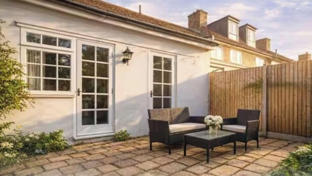 A patio with a table and chairs, a white building with windows and a door, and a wooden fence. - 3BR Putney Home London Sleeps 8 Winter Deal (London)