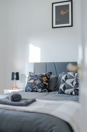 A modern bedroom with a grey headboard, patterned pillows, and a framed artwork on the wall. - 3BR Putney Home London Sleeps 8 Winter Deal (London)