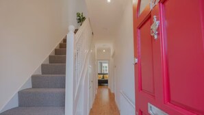 A hallway with a staircase on the left and a red door on the right. - 3BR Putney Home London Sleeps 8 Winter Deal (London)