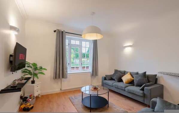 A modern living room with a grey sofa, a round coffee table, a potted plant, and a TV on a stand. - 3BR Putney Home London Sleeps 8 Winter Deal (London)