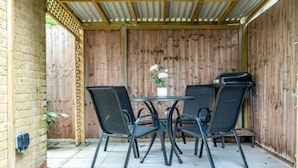 Une terrasse extérieure dotée d’une pergola en bois, d’une table avec quatre chaises et d’un barbecue.