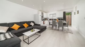 Un salon moderne avec un canapé noir, une table basse blanche et un coin cuisine doté de meubles blancs et d’une table à manger.
