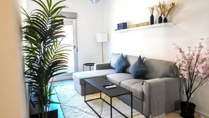 Una sala de estar moderna con un sofá gris, una mesa de centro negra, una planta grande en maceta y una mesita auxiliar.