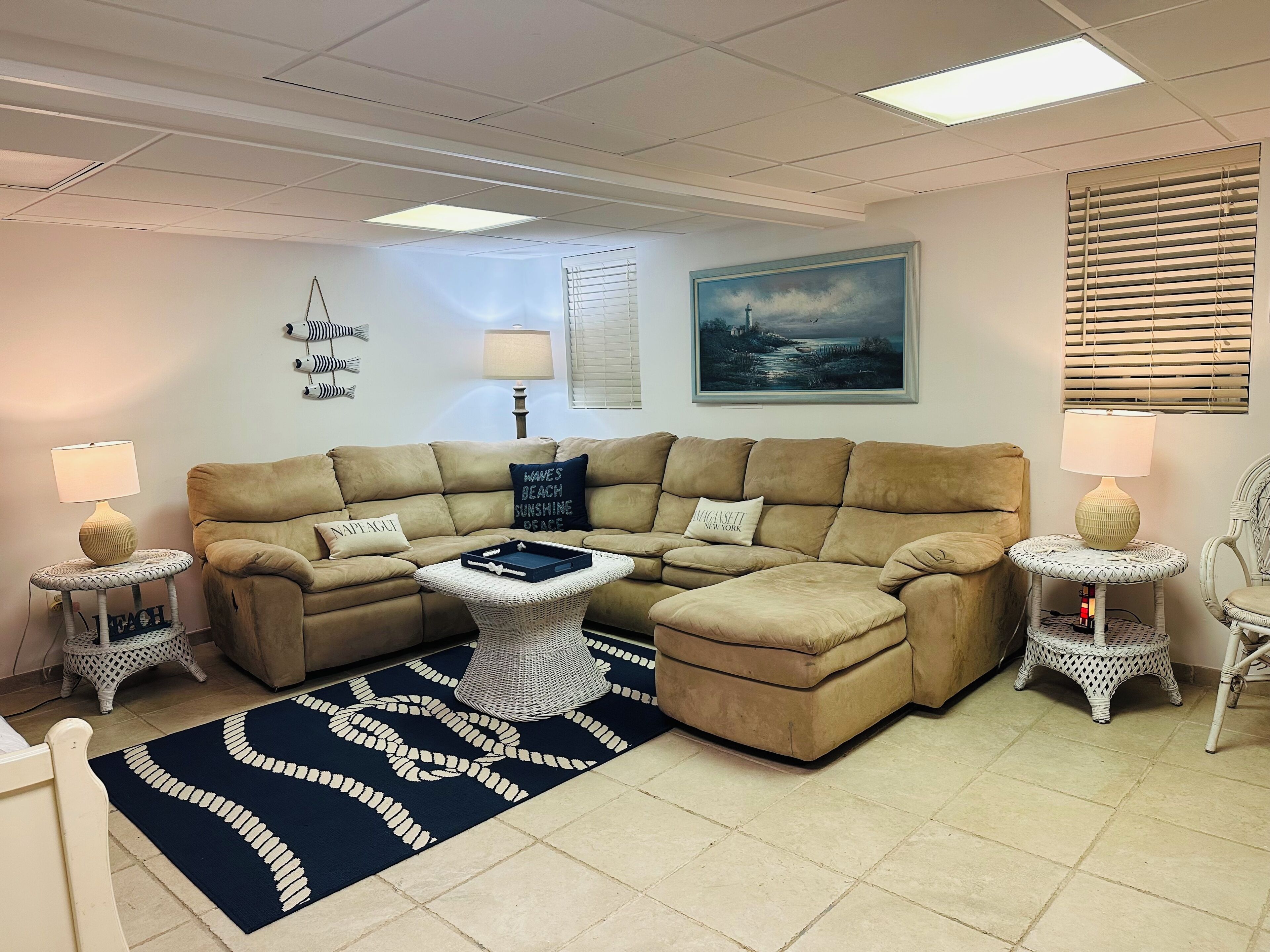 A living room with a beige sectional sofa, a round coffee table, two side tables with lamps, a blue and white patterned rug, and a painting on the wall.