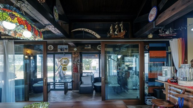 A room with a wooden table, chairs, a glass door leading outside, and a ship model on the wall.