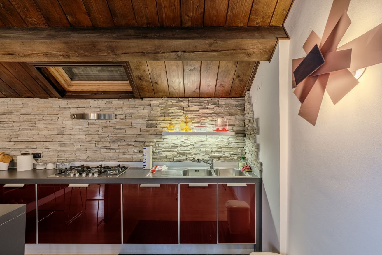 A kitchen with a stone wall backsplash, a gas stove, and a modern pendant light.