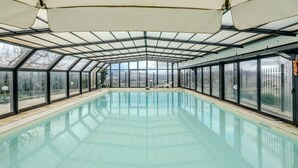 A covered swimming pool with glass walls and a roof, surrounded by a fence.