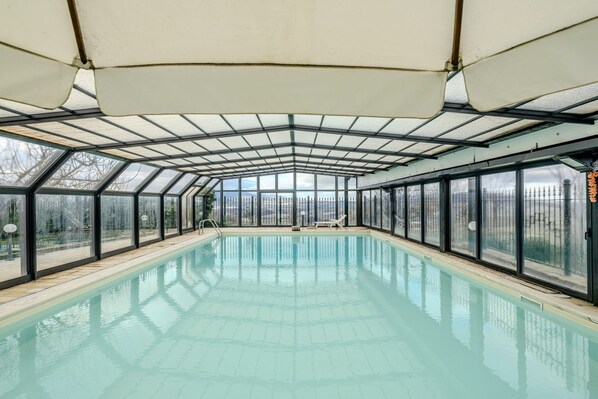 A covered swimming pool with glass walls and a roof, surrounded by a fence.