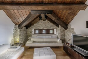 Une pièce de style loft avec des poutres en bois apparentes, un mur en pierre, un canapé blanc, une télévision et une petite table avec une lampe.