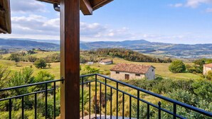 A balcony with a view of a rural landscape, including fields and distant hills.