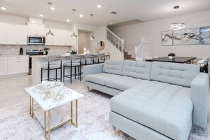 A modern kitchen with white cabinets, a central island with bar stools, and a dining area with a light blue sofa. - 5BR Windsor Cay Home with Clubhouse (Clemornt)