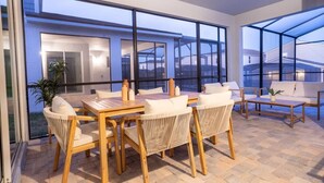 En moderne udendørs terrasse med et træbord og stole, store vinduer og udsigt til de omkringliggende bygninger.