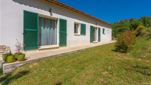 Un edificio blanco con contraventanas verdes, techo de tejas y un área ajardinada con macetas.