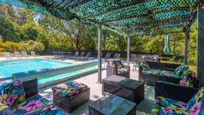 Area piscina con sedie a sdraio, una piscina e una zona relax coperta con mobili in vimini.