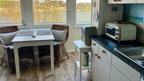 Una cocina con vista a un cuerpo de agua, una zona de comedor con muebles de mimbre y un armario blanco con un tostador.
