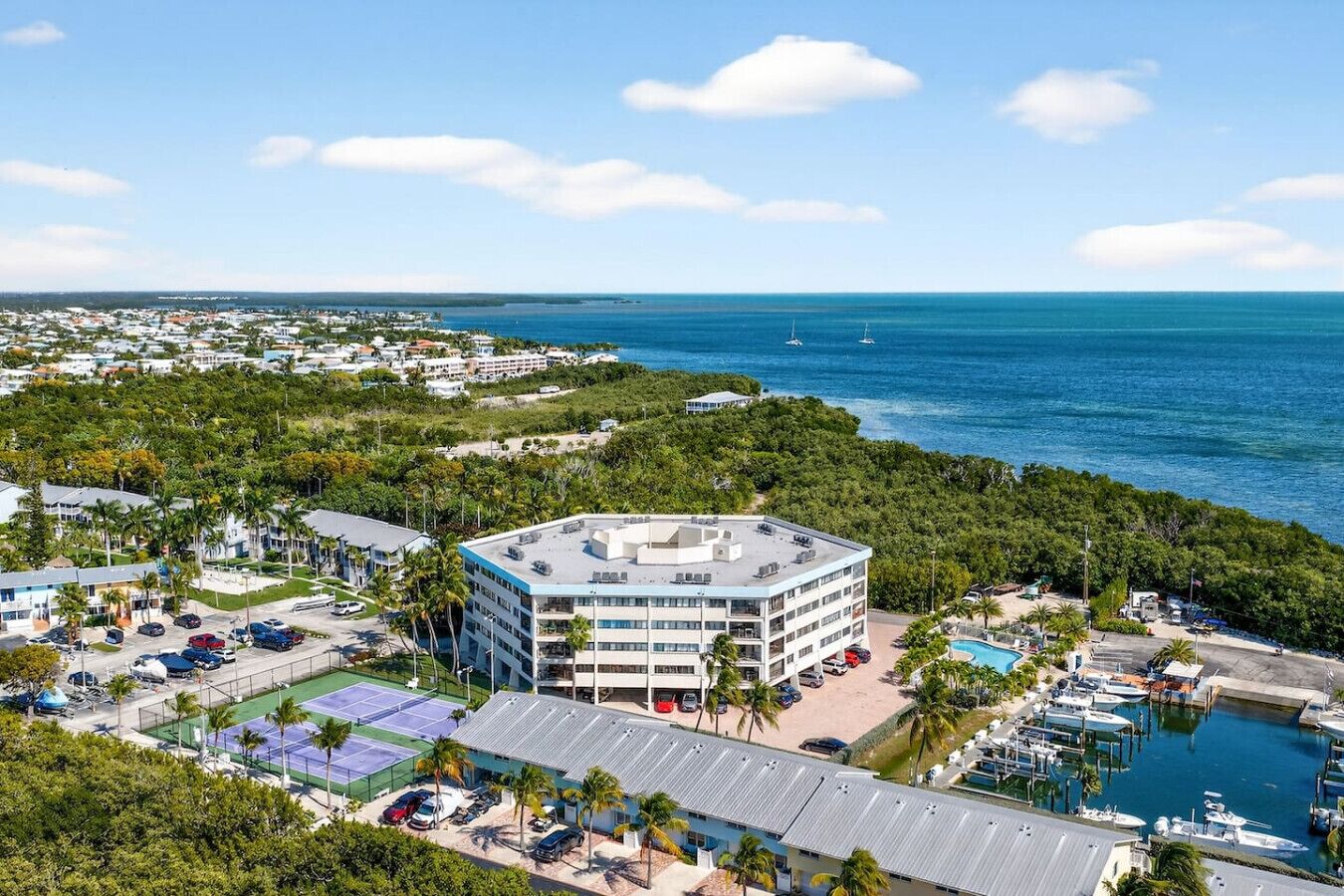 A multi-story hotel with a rooftop pool, surrounded by lush greenery and a marina.