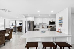 A modern kitchen with white cabinetry, stainless steel appliances, and a central island with stools. - Kawama, Key Largo, Oceanfront Stay, Marina & Pool (Key Largo)