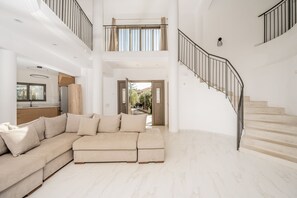 Ein großzügiger Wohnbereich mit einem beigefarbenen Ecksofa, einer Treppe und Blick ins Freie.