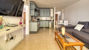 Una cocina moderna con armarios azul claro, una zona de comedor con sofá gris y un banco de madera.