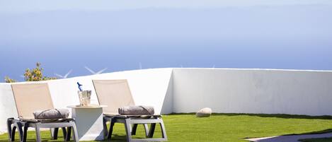 A pool area with two lounge chairs, a small table with a drink, and a view of the ocean.