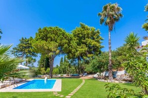 A swimming pool surrounded by a well-maintained lawn, trees, and a clear blue sky. - Villa Hacienda Zante (Zakynthos)