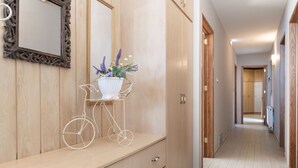 Un corridoio con pareti in legno intarsiato, uno specchio, uno scaffale bianco con una pianta e un supporto a forma di bicicletta.