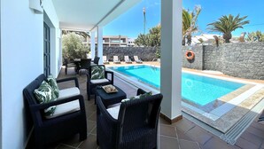 A covered outdoor area with a pool, lounge chairs, and a stone wall. - Your Island Villa Mamma Mia 1 (Yaiza)