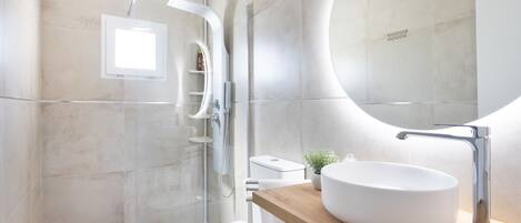 Un baño moderno con un espejo grande, un lavabo redondo y una zona de ducha.
