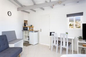 A modern living room with a grey sofa, a white dining table with two chairs, a small kitchen area with a microwave, and a TV on a stand. - Oasis Tenerife Studio 4 (Granadilla de Abona)