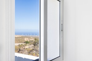 A window with a view of a coastal landscape, including vegetation and distant wind turbines. - Oasis Tenerife Studio 4 (Granadilla de Abona)